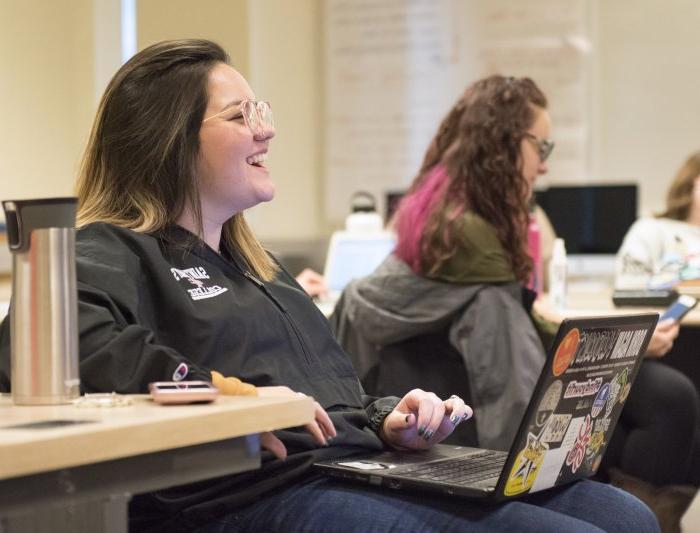 Woman laughs while using her computer in a classroom